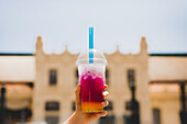 Hand of anonymous female holding takeaway cup of tasty ice juice against street background