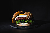Tasty burger with egg placed on patty and fresh lettuce served on slate board on black background in studio