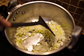Blick von oben auf einen nicht erkennbaren Koch, der gehackten Knoblauch und Zwiebeln in einer Metallpfanne brät, während er in einer Küche zu Hause Essen zubereitet