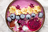 From above of power bowl full of tasty smoothie near ripe banana and dragon fruit slices with blueberries for breakfast
