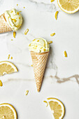 Draufsicht auf köstliche Eiskugeln in Waffeltüten, die auf einem Marmortisch in der Nähe von Zitronenscheiben und -schalen in der Küche angeordnet sind