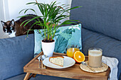 Tasse Kaffee und hausgemachter Biskuitkuchen auf einem Holztablett mit einem Glas frischem Orangensaft zum Frühstück im Wohnzimmer