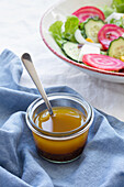 Hochformatiger Löffel in Glasschale mit Honig auf Tisch neben vegetarischem Salat mit Gurke und Roter Bete mit grünen Blättern und Mais