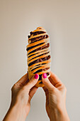 Hands of woman with bright pink manicure holding tasty baked azuki bun on grey background