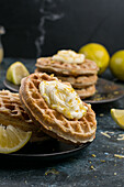 Pile of tasty homemade sweet baked chaffles served on black plate with lemon and zest on table in light kitchen