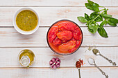 Draufsicht auf geschälte Tomaten auf Holztisch mit Olivenöl und Basilikumblättern neben Knoblauch und verschiedenen Gewürzen für Marinara-Sauce