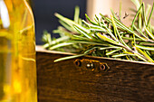 Rosmarinzweige mit grünen Blättern in einer kleinen Holztruhe neben einer Glasflasche mit Öl auf der Oberfläche an einem hellen Ort