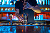 Hands of unrecognizable bartender at work stirring a cocktail in his shaker in the bar