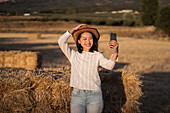 Frau fotografiert mit dem Handy, während sie im Sommer bei Sonnenuntergang in einem getrockneten Feld steht