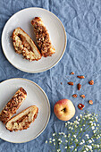 Overhead view of yummy apple pastry on ceramic saucers near fresh fruit and crunchy pecan nuts with flower on creased textile