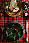 Von oben weihnachtlich gedeckter Tisch mit Kranz auf Keramikteller mit Besteck auf rot-kariertem Tischtuch im Hintergrund