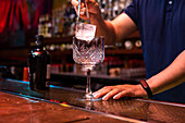 Unrecognizable bartender putting a big ice cube into the glass while preparing a gin tonic cocktail in the bar