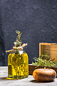 Glasflasche mit ätherischem Öl, Rosmarinzweigen und brennender Bio-Holzkerze auf grauem Tisch