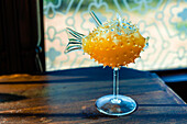 Creative fancy bright yellow alcoholic drink served in fugu fish cocktail glass on wooden bar counter