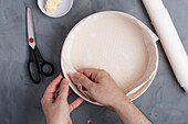 From above of crop unrecognizable female putting baking paper on bakery form while preparing cake