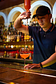 Young Asian bartender pouring grapefruit juice in the glass while preparing a cocktail in the bar
