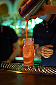 Detail of unrecognizable bartender's hand working in the bar with his shaker and pouring a cocktail in the glass