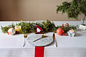 Von oben auf einen weihnachtlich gedeckten Tisch mit Kranzdekoration, rot und weiß, mit goldenem Besteck und Kerzen