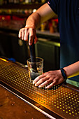 Unbekannter Barkeeper zerdrückt Zitronenspalten im Glas bei der Zubereitung eines Mojito-Cocktails in der Bar