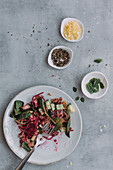Draufsicht auf Teller und Schale mit leckerem Linsensalat mit Gurken und Spinat neben Servietten auf grauem Tisch