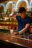 Young Asian bartender pouring rum in the glass while preparing mojito cocktail in the bar