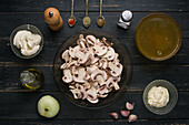 Draufsicht auf verschiedene Zutaten für Pilzsuppe mit Zwiebeln und Brühe auf Holztisch mit Gewürzen in Küche