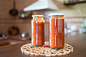 Tasty homemade marinara sauce from tomatoes in glass jars placed on wooden table in kitchen
