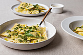 Appetizing cooked ravioli pasta with green sauce and herbs placed on white plates with forks on table