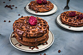 Von oben: leckere süße Waffeln mit Schokoladensauce und Himbeeren, serviert auf einem Tisch mit Schokoladendrops in einer hellen Küche