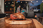 Leckeres gegrilltes Schweinefleisch mit knuspriger Kruste, serviert auf einem hölzernen Schneidebrett auf einem Tisch in einem hellen Café mit professioneller Ausstattung