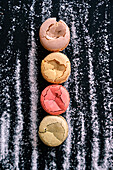 Draufsicht auf farbige Kekse auf schwarzem Hintergrund, umgeben von Zuckerstreifen