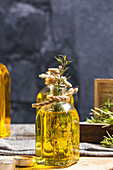 Glasflasche mit ätherischem Öl, Rosmarinzweigen und brennender Bio-Holzkerze auf grauem Tisch