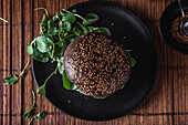 Appetizing burger with sesame seeds placed on black plate near salad leaves