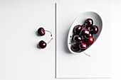 High angle of healthy ripe tasty cherries in ceramic bowl placed on white board