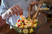 Crop female putting fresh shrimps on top of salad in glass bow in kitchen at home