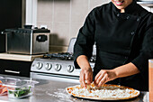 Cropped unrecognizable female chef in uniform cooking delicious pizza on kitchen counter
