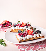 From above tasty sweet puff pastry tart with whipped cream and fresh berries served on plate near green mint leaves