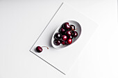 High angle of healthy ripe tasty cherries in ceramic bowl placed on white board