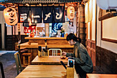 Junge asiatische Frau im Pullover isst an einem Holztresen in einem Cafe