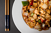 Overhead view of dish of delicious Gong Bao chicken against black background in restaurant