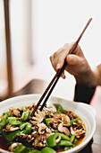 Eine Hand isst eine Schüssel mit heißer, köstlicher Suppe mit würzigem Oktopus und Gurke mit Stäbchen in einem asiatischen Café