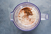 Top view of bowl of blender with mixed ingredients for milkshake with ground cinnamon and cubes of ice