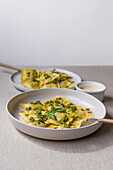 Appetitlich gekochte Ravioli Nudeln mit grüner Soße und Kräutern auf weißen Tellern mit Gabeln auf dem Tisch