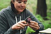 Woman sitting at table and cutting fresh mushroom against green grass in nature