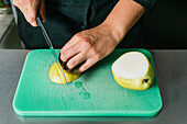 Anonymer Koch schneidet frische reife Birne mit einem scharfen Messer in der Küche eines Restaurants auf einem Plastikschneidebrett auf