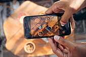 From above of crop anonymous ethnic person taking picture of instant photo camera and glasses of cocktails on table