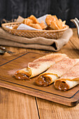 Frisch gerollte Crêpes mit süßer Dulce de Leche-Füllung, serviert auf einem hölzernen Schneidebrett auf einem Tisch mit Wasserkocher in der Küche
