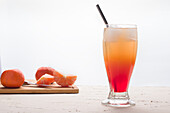 Glas erfrischender Sunrise-Cocktail mit Eiswürfeln und Strohhalm, serviert auf einem Tisch mit frischen Orangen