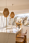 Innenansicht eines Essbereichs in einer gemütlichen, hellen Küche mit Bambuslampen über dem Tisch und Holzstühlen in der Nähe des Fensters