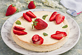Tasty round shaped cheesecake decorated with ripe strawberries and green mint leaves served on plate on table in light kitchen